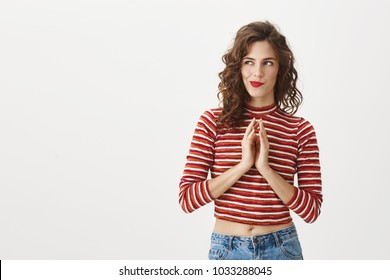 I have great idea. Studio shot of attractive female moving fingers near chest as if making up plan in mind, smiling mysteriously while looking aside, wanting to do something illegally or secretly
