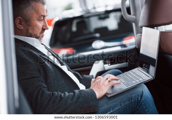 Have job even on the road.\
Working on a back of car using silver colored laptop. Senior\
businessman.