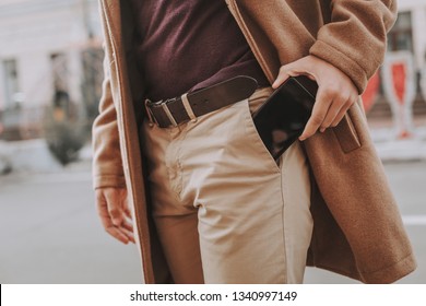 I have to make a phone call. Close up of elegant guy taking modern black cellphone out of trouser pocket