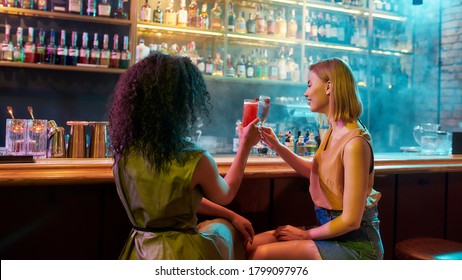 Have A Nice Night. Two Women Having Fun, Toasting, Drinking Cocktails While Sitting At The Bar Counter. Friends Spending Time At Night Club, Restaurant. Selective Focus On Woman. Web Banner