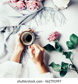 Having a break: female hands holding cup of coffee. Flatlay with wool scarf and pink roses. Overview.