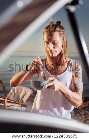 Having breakfast. Man with long blonde hair and tattoo having delicious breakfast near his mobile home