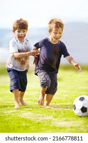 Having a friendly game. Two cute little boys playing soccer together outside while covered in mud.