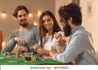 Having Fun At Casino Themed Party. Smiling Young Woman Playing Poker Board Game With Young Men Sitting At Table With Some Drinks At Home Or In Club