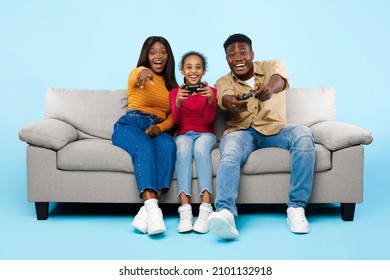 Having Fun. Excited African American Family Playing Video Games Together With Controller, Holding And Using Joysticks Over Blue Studio Background Sitting On Couch, Banner. Free Time Entertainment