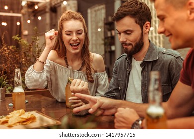 Having fun with friends. Charming long-haired nice-appealing young woman and two happy laughing attractive guys having fun and playing games at the bar