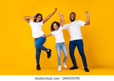 Having Fun. Full body length of excited young black family of three dancing and fooling around. Happy African American man, woman and girl enjoying favorite music together on yellow studio background