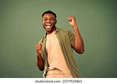 Having fun. Happy african american guy joyfully dancing and fooling around over green studio background. Handsome smiling man dressed in casual attire enjoying carefree youth lifestyle. - Powered by Shutterstock