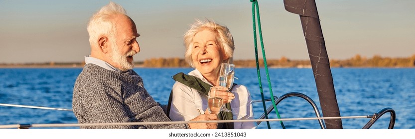 Having fun. Happy beautiful senior family couple drinking wine or champagne and laughing while relaxing on a sailboat or yacht deck floating in a calm blue sea - Powered by Shutterstock