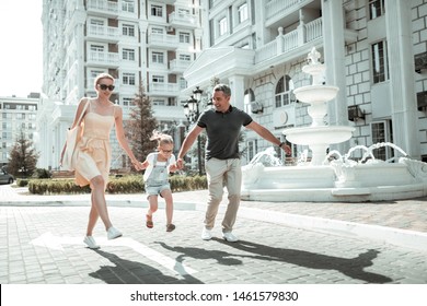 Having Fun. Happy Nuclear Family Holding Hands Skipping Together Along The Street With The Beautiful Architecture.