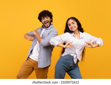 Having fun. Joyful young indian couple dancing and fooling around, enjoying favorite national music together on yellow studio background - Shutterstock ID 2105072612