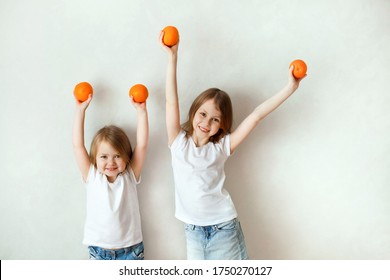 Having Fun Kids Girls Siblings With Orange Citrus Fruits In Their Hands On A White Background. The Concept Of Summer, Healthy Food, Juices, Vitamins For Children. Soft Focus.