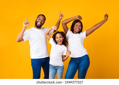 Having Fun. Portrait of excited young black family of three dancing and fooling around. Happy African American man, woman and girl enjoying favorite music together on yellow studio background