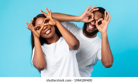 Having Fun. Portrait of joyful black couple smiling, looking at the camera through fingers, doing okay gesture and covering eyes, imitating eyeglasses. Facial expressions and emotions concept