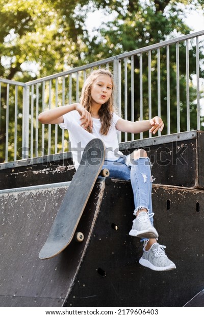 Having fun\
with skate board. Funny child girl with skate sitting on sport\
ramp, smiling and grimacing on skate playground. Active teenager\
posing with skate board. Extreme\
lifestyle