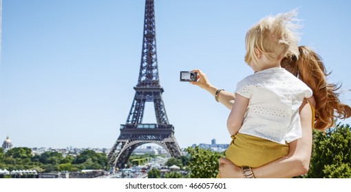 Having Fun Time Near The World Famous Landmark In Paris. Seen From Behind Mother And Child Taking Photo With Digital Camera Against Eiffel Tower