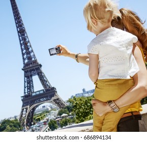 Having Fun Time Near The World Famous Landmark In Paris. Seen From Behind Mother And Child Taking Photo With Digital Camera Against Eiffel Tower