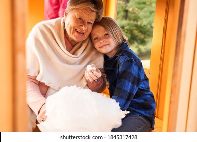 Having Fun Together. Cheerful Grandmother And Her Blonde Attractive Grandson Laying With Head On Her Shoulder Eating Cotton Candy At The Kid Train At The Park