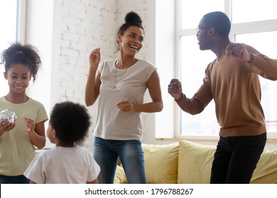 Having Fun Together. Happy Active Black Family, Married Couple And Kids Daughter And Son Jumping, Singing And Laughing In Living Room, Cute African Mom, Dad And Two Little Children Dancing At Home