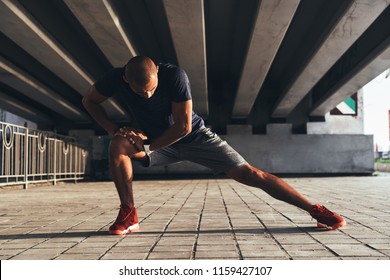 Having a good stretch. Handsome young African man in sports clothing stretching while warming up outdoors - Powered by Shutterstock