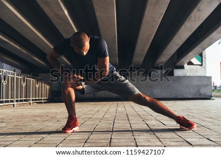 Having a good stretch. Handsome young African man in sports clothing stretching while warming up outdoors
