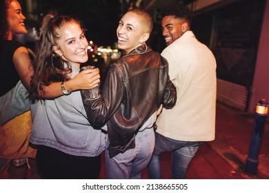 Having A Good Time On A Saturday Night. Rearview Of A Group Of Vibrant Friends Laughing Happily While Walking In The City At Night. Multicultural Friends Going Out Together On The Weekend.