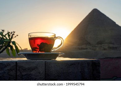 Having mint tea at an cafe while contemplating the impressive three pyramids of Giza. Transparent glass mug with black tea and mint on the background of the Egyptian pyramids.