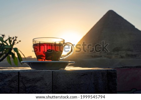Having mint tea at an cafe while contemplating the impressive three pyramids of Giza. Transparent glass mug with black tea and mint on the background of the Egyptian pyramids.