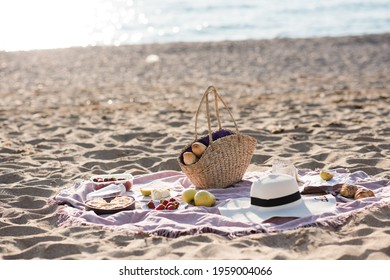 Having Picnic With Fresh Bread, Straw Bag And Hat On Blanket At Sandy Beach Over Sea Shore At Background. Summer Season. Vacation Time. 