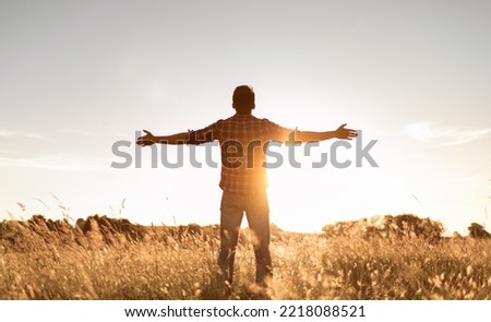 Having a positive mindset, wellbeing and hope concept. Happy young man standing in a nature sunrise field with arms outstretched.	