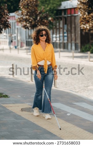 Having a walk, using white cane. A blind woman is in the modern city at daytime.