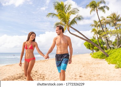 Hawaii beach vacation couple walking happy on Kaanapali beach, Maui, Hawaii, USA. Two people man, Asian bikini woman relaxing on stroll famous hawaiian destination for summer travel holidays.