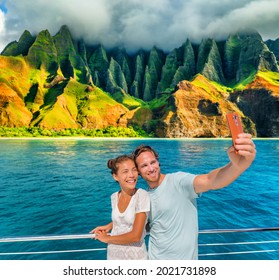 Hawaii Cruise Ship Couple Tourists Taking Selfie Photo With Phone At Na Pali Coast, Kauai Island, USA Summer Vacation Travel. Happy Asian Woman, Caucasian Man, Interracial Friends Group Of People.