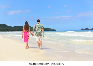 Hawaii Honeymoon Couple Of Newlyweds Walking On Tropical Beach In Hawaiian Apparel, Pink Sarong Dress And Green Aloha Shirt For Polynesian Cultural Tradition. Young People Holding Hands Happy In Love.