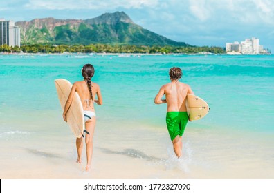Hawaii Honolulu couple surfers going surfing on waikiki beach with surfboards running in water. Healthy active sport lifestyle fitness people at diamond head mountain landscape.