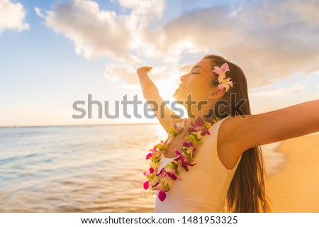 Hawaii hula luau woman wearing hawaiian lei flower necklace on Waikiki beach dancing with open arms free on hawaiian vacation. Asian girl with fresh flowers hair, traditional polynesian dance.