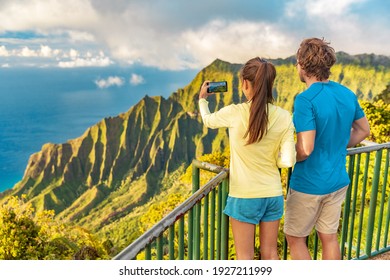 Hawaii Kauai Island Travel Tourists Couple Taking Phone Picture Of Na Pali Coast Mountain Range At Sunset. USA Famous Vacation Destination.