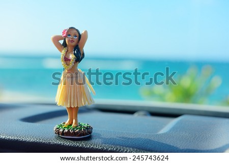 Hawaii road trip - car hula dancer doll dancing on the dashboard in front of the ocean. Tourism and travel freedom concept.