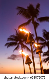 Hawaii Sunset With Lit Tiki Torches. Hawaiian Icon, Lights Burning At Dusk At Beach Resort Or Restaurants For Outdoor Lighting And Decoration, Cozy Atmosphere.