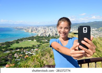 Hawaii Tourist Taking Selfie Photo Of Honolulu And Waikiki Beach Using Smartphone. Woman On Hike Visiting Famous Viewpoint Lookout In Diamond Head State Monument And Park, Oahu, Hawaii, USA.