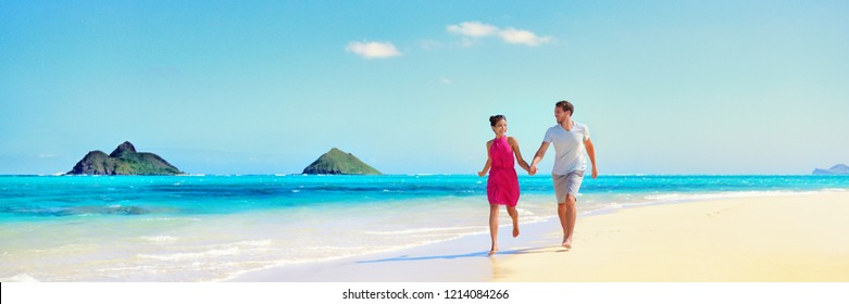 Hawaii vacation couple walking relaxing on white sand and pristine turquoise ocean water on Hawaiian beach Lanikai, Oahu island, USA. Holiday background with blue sky copy space for travel concept.