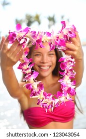 Hawaii woman showing flower lei garland of pink orchids. Beautiful smiling mixed race woman in bikini on beach giving a welcoming Lei on the hawaiian island Big Island.