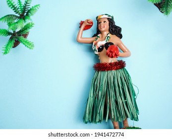 Hawaiian Hula Girl Doll With Plastic Palm Trees Against Sky Blue Background