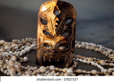 Hawaiian Mask Sticks Out Of Beach Surrounded By Shell Necklaces