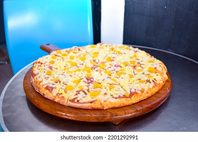 Hawaiian Pizza On A Wooden Base On A Metal Table In A Restaurant