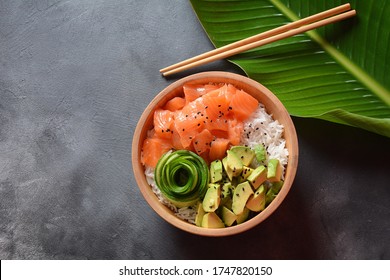 Hawaiian Salmon Poke Bowl with  avocado, cucumber , rice and sesame seeds served in bowl on tropical leaves. Sushi bowl.Organic and healthy food. 