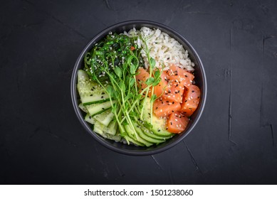 Hawaiian salmon poke bowl with seaweed, avocado, sesame seeds and cucumber on black background. Top view, flat lay