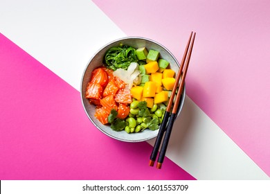 Hawaiian salmon poke bowl with seaweed, avocado, edamame, mango and pickled ginger. Top view, bright pink background