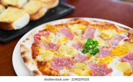 Hawaiian Thin Crisp Pizza Has Pineapple Ham Cheese And Dill On Top With Garlic Bread On White Dish And Black Tray For Lunch Or Breakfast And Dinner For Family Eating Food At Italian Cuisine Restaurant