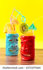 Hawaiian Tiki Bar, Summer Refreshing Drinks And Tropical Cocktails Concept Theme With Glasses Of Alcohol And Juice Mixed Together, Kiwi And Orange Slices, Umbrella And Drinking Straw On Wooden Table